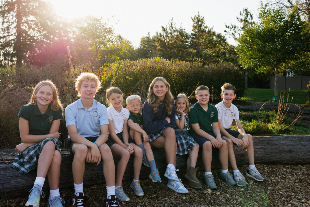 Group of eight school children sitting on a log outdoors during golden hour