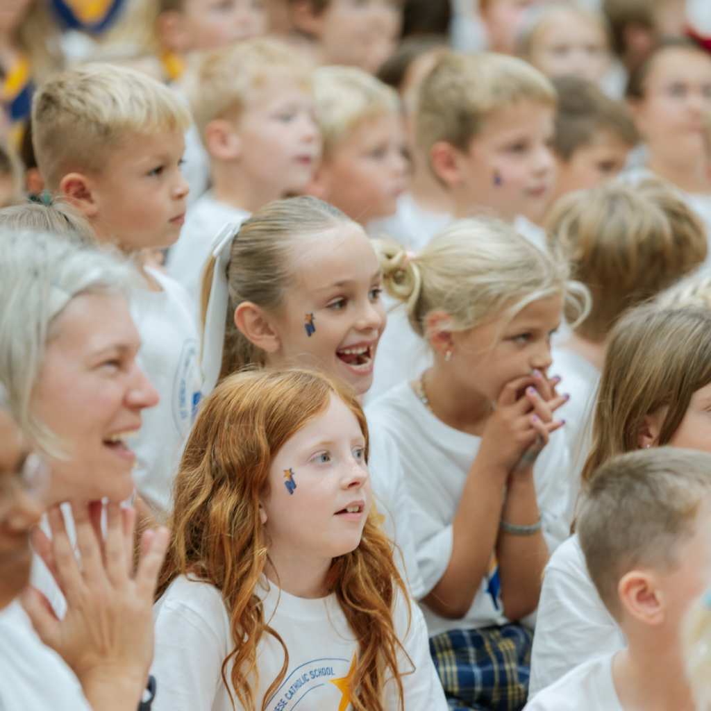 Group of young school children in white uniforms at a school event or assembly.