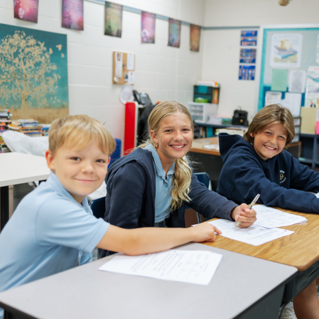 Three smiling students working together at desks in a colorful classroom setting.